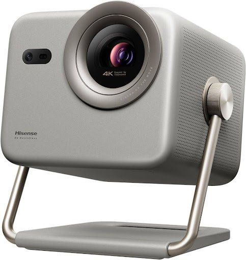 "A front-three-quarter view of a Hisense 'Be Boundless' 4K projector. The device has a matte silver finish, a prominent lens labeled 'Powered by TriChroma,' and a dual-sensor array. It is supported by a modern metal stand with a textured adjustment knob on the side, designed for portability and adjustable viewing angles."