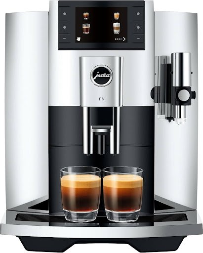 "The front of the silver and black Jura E8 espresso machine, displaying the color touchscreen and two cups of fresh espresso under the double tap, highlighting the side milk steaming system."